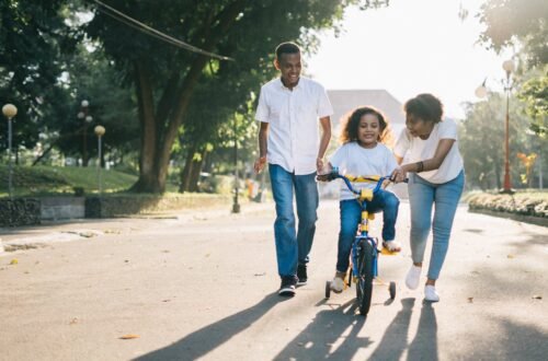 man standing beside his wife teaching their child how to ride bicycle